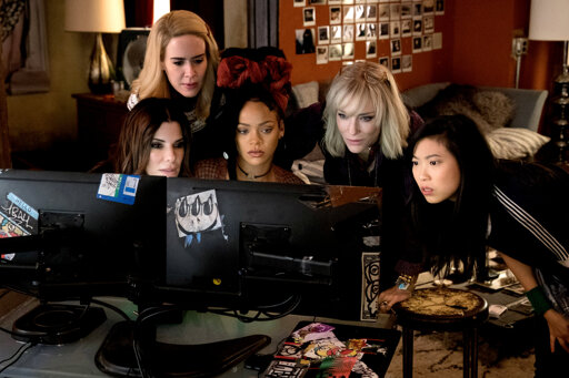 Promotional image from Ocean's 8. Five women stare intently at side-by-side computer monitors.